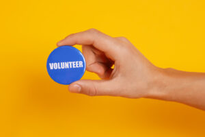 Man holding button badge with word Volunteer on orange backgroun